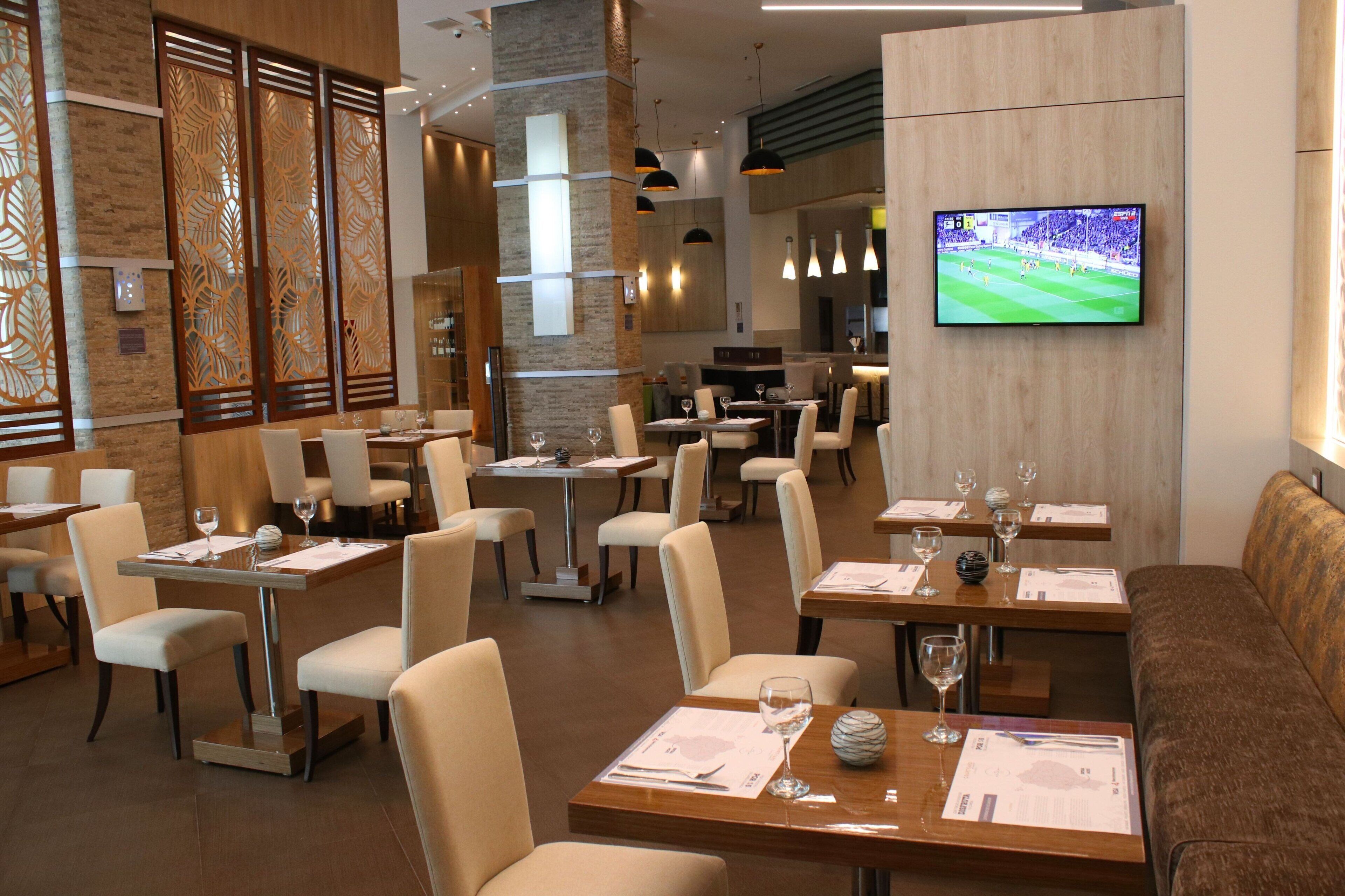 Ein modernes Restaurant mit mehreren Tischen und Stühlen, einem an der Wand befestigten Fernseher und dekorativen Holzpaneelen.