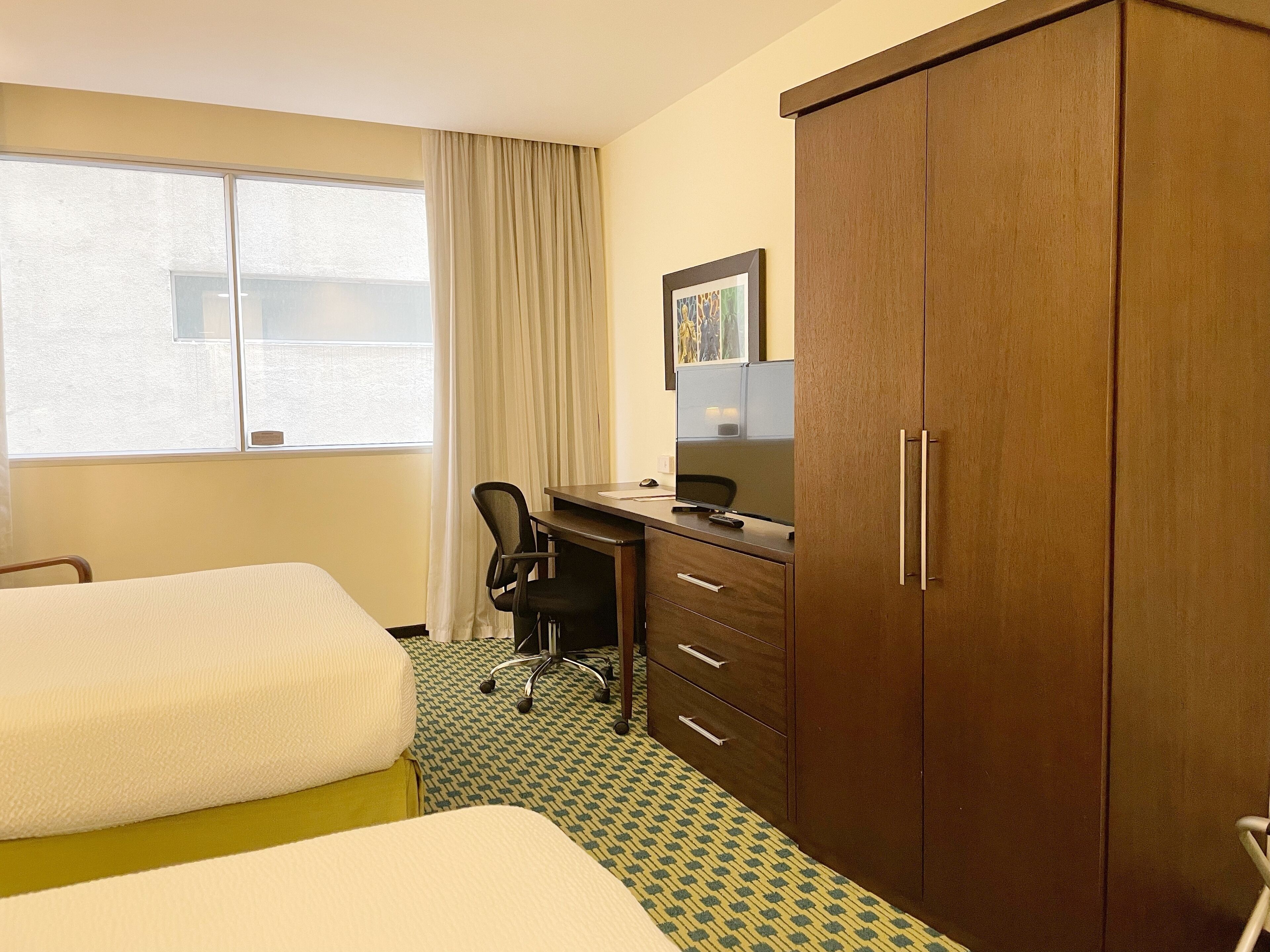 Une chambre d’hôtel avec deux lits, un bureau avec un ordinateur, une chaise et une armoire.