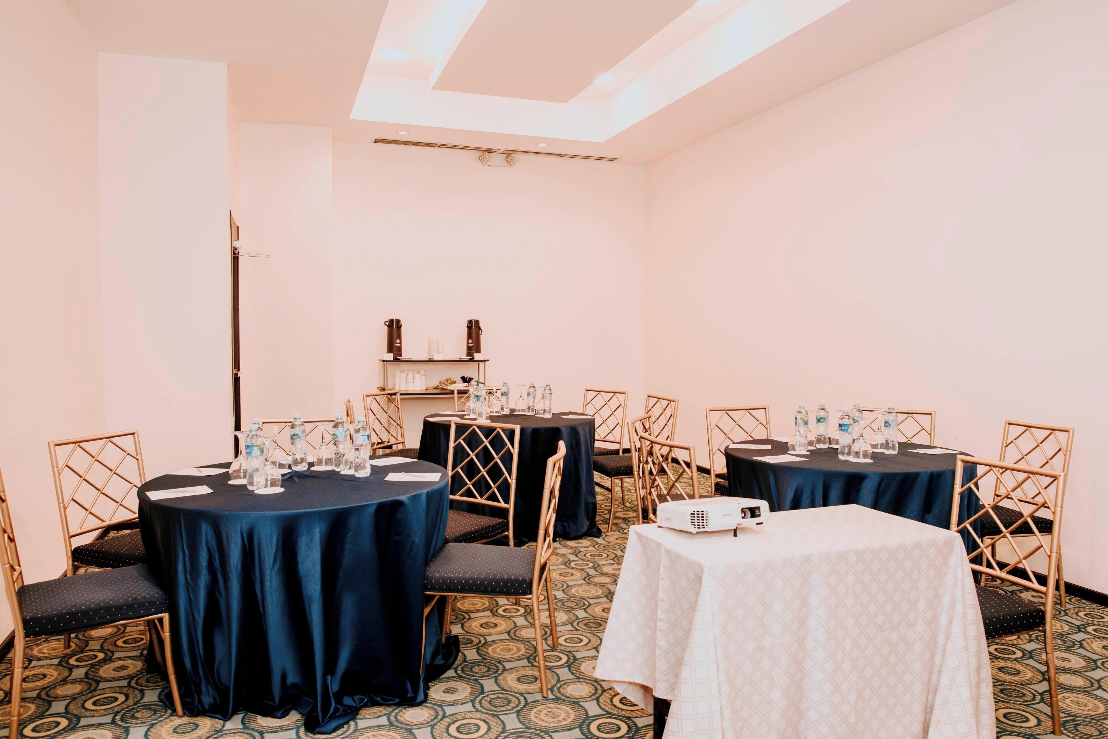 Un salón de conferencias con mesas redondas, sillas y un proyector.
