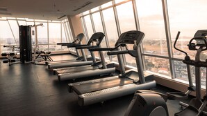 Un gimnasio con cintas de correr y equipo de ejercicio, ventanas amplias y vistas a un paisaje urbano.