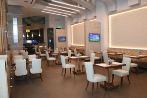 Um restaurante moderno com várias mesas e cadeiras, um bar e uma tela grande exibindo um evento esportivo.
