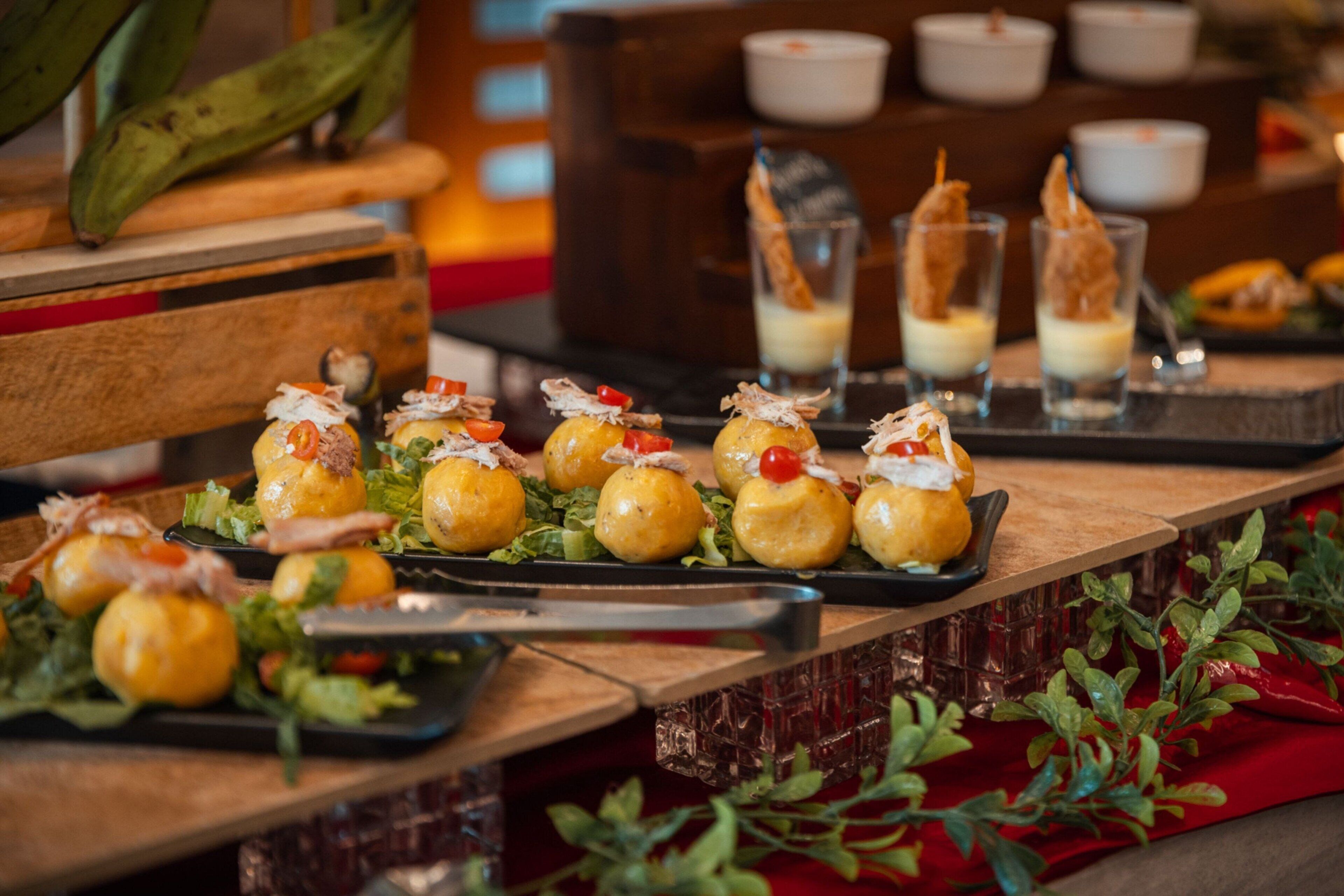 Una mesa de buffet con varios platos, incluyendo pequeñas piezas redondas decoradas con adornos, y vasos con una bebida cremosa.