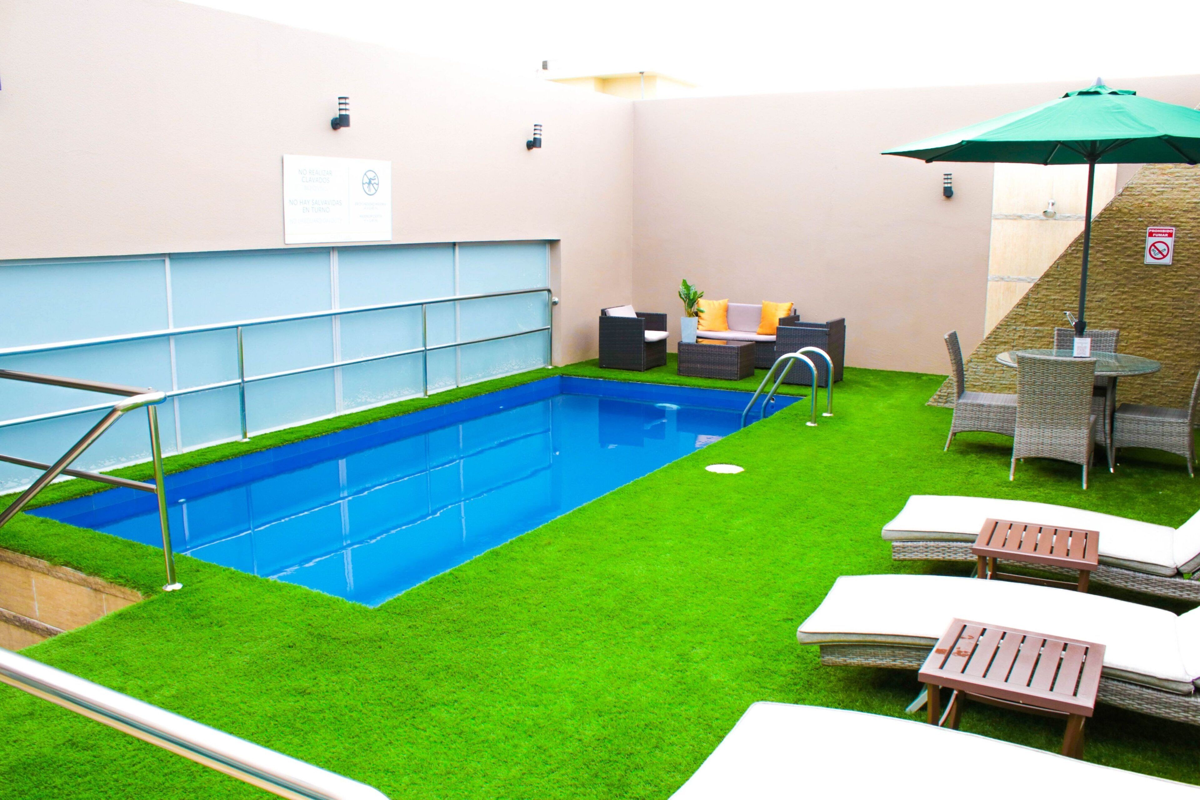Una piscina con césped artificial, sillas de descanso y una pequeña mesa con sombrilla.