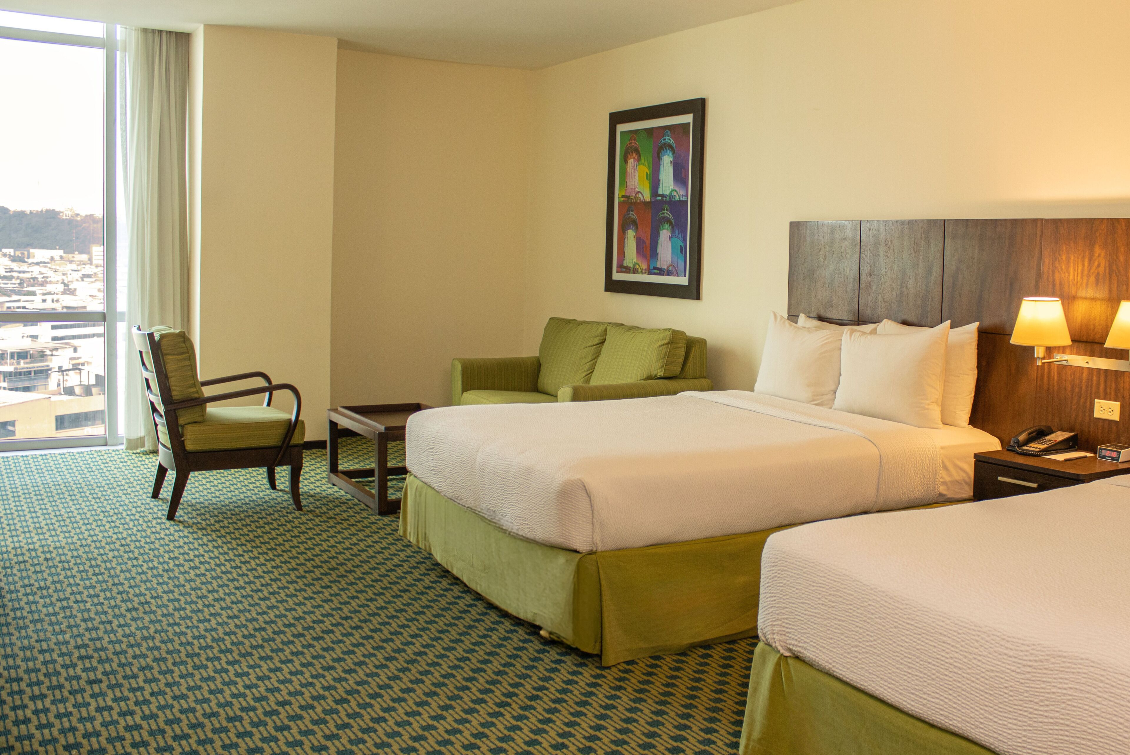 A hotel room with a large bed, a smaller bed, a chair, a desk, and a painting on the wall.