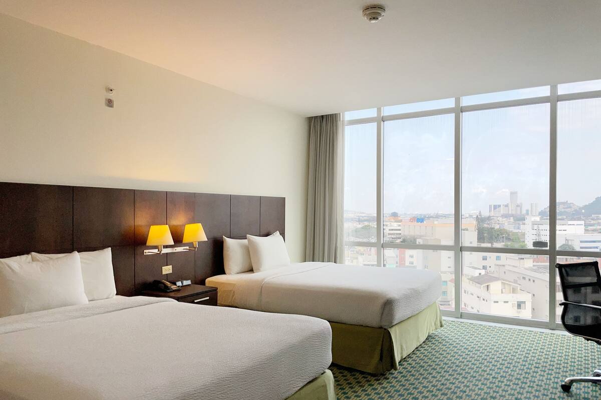 Une chambre d’hôtel avec deux lits, une grande fenêtre et une vue sur la ville.