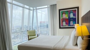 Habitación de hotel con una cama grande, una silla, un cuadro y vistas a la ciudad.