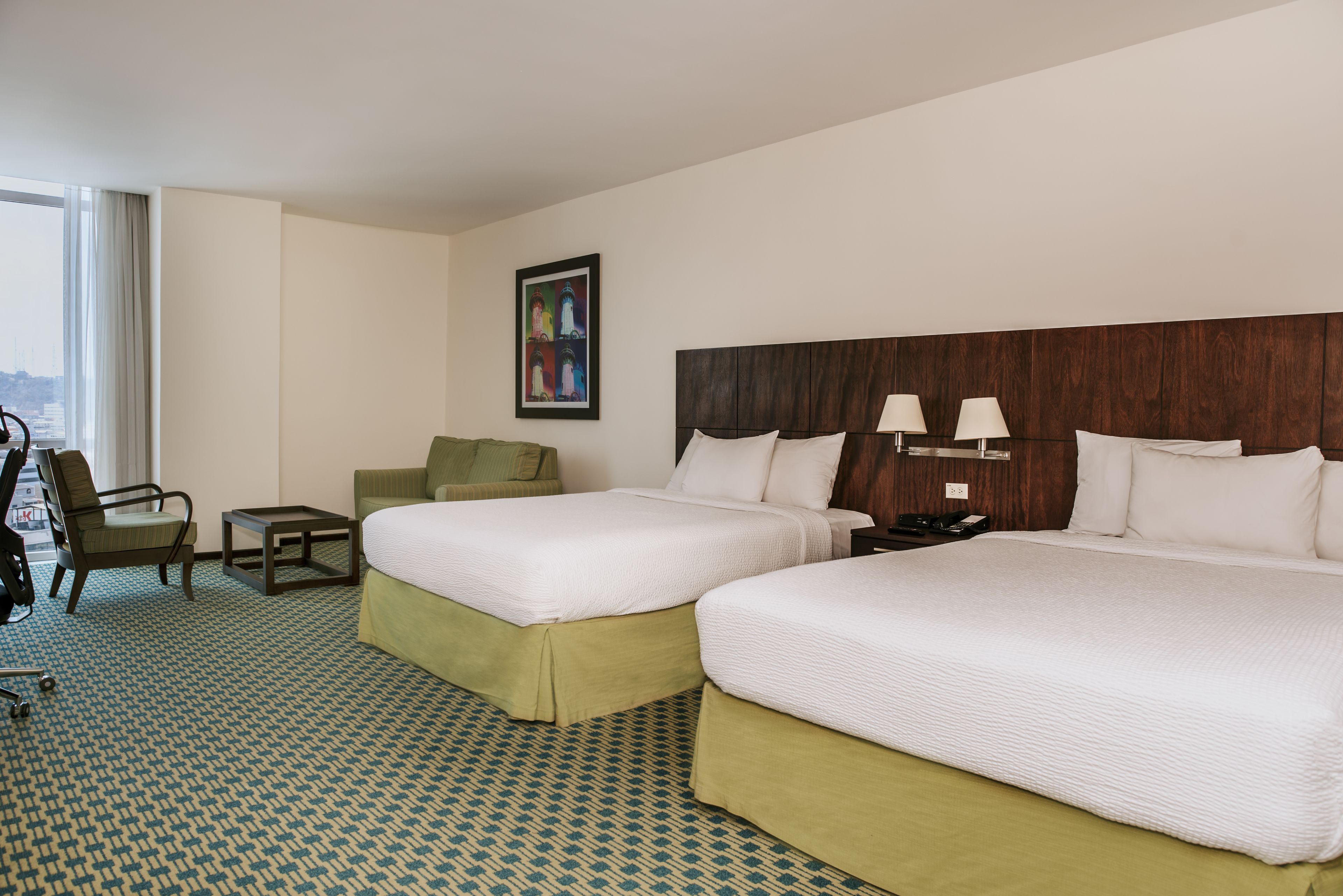 Ein Hotelzimmer mit zwei Betten, einem Sessel, einem kleinen Tisch und einem Bild an der Wand.