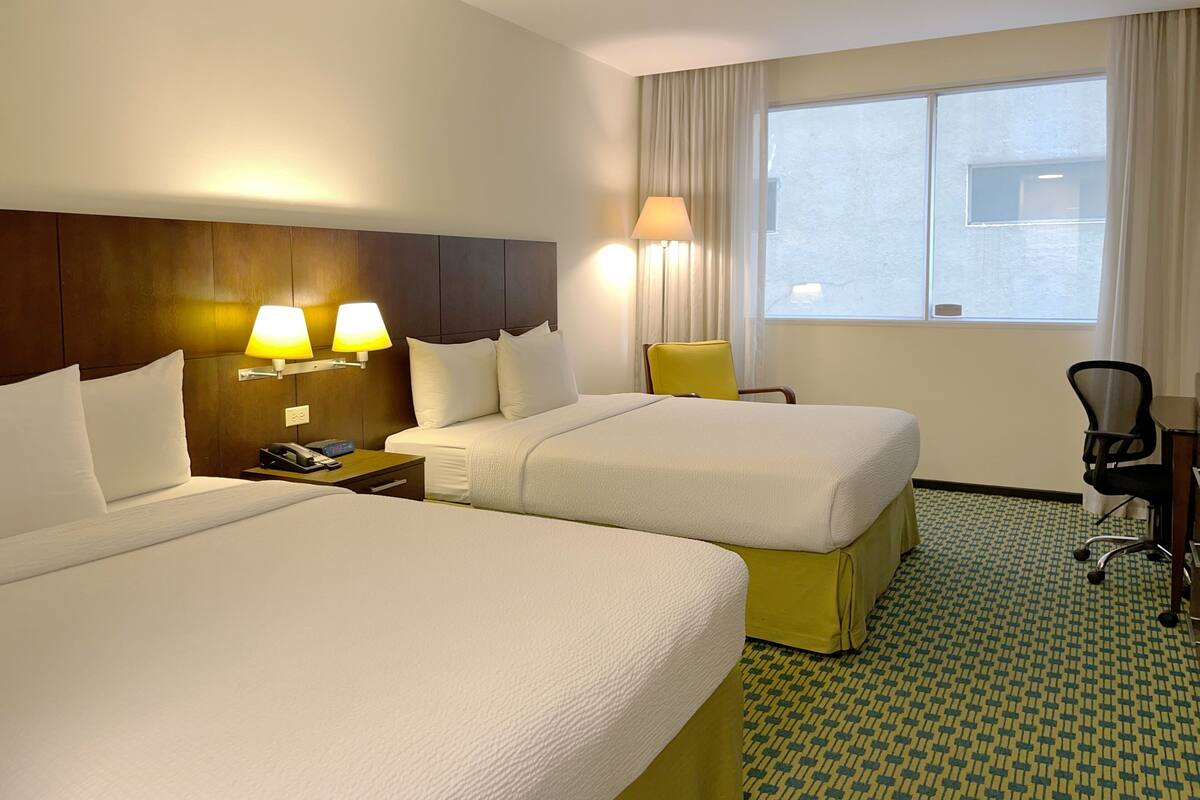 Une chambre d’hôtel avec deux lits, un bureau, une chaise, une lampe et une fenêtre.