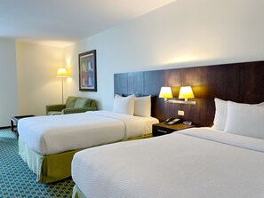 Quarto de hotel com duas camas, uma mesinha de cabeceira com telefone e relógio digital, uma poltrona verde, um abajur e um quadro na parede.