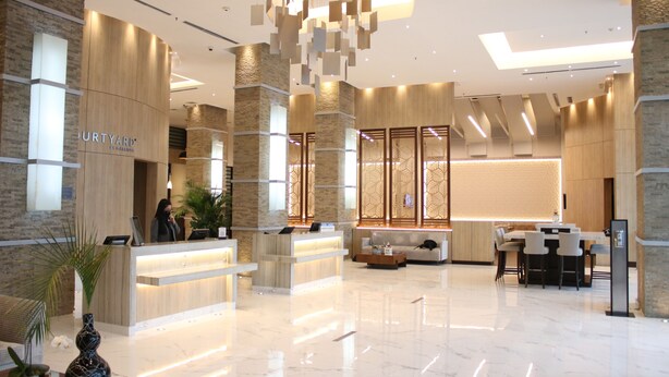 Un moderno vestíbulo de hotel con mostrador de recepción, zona de estar y una gran planta decorativa.