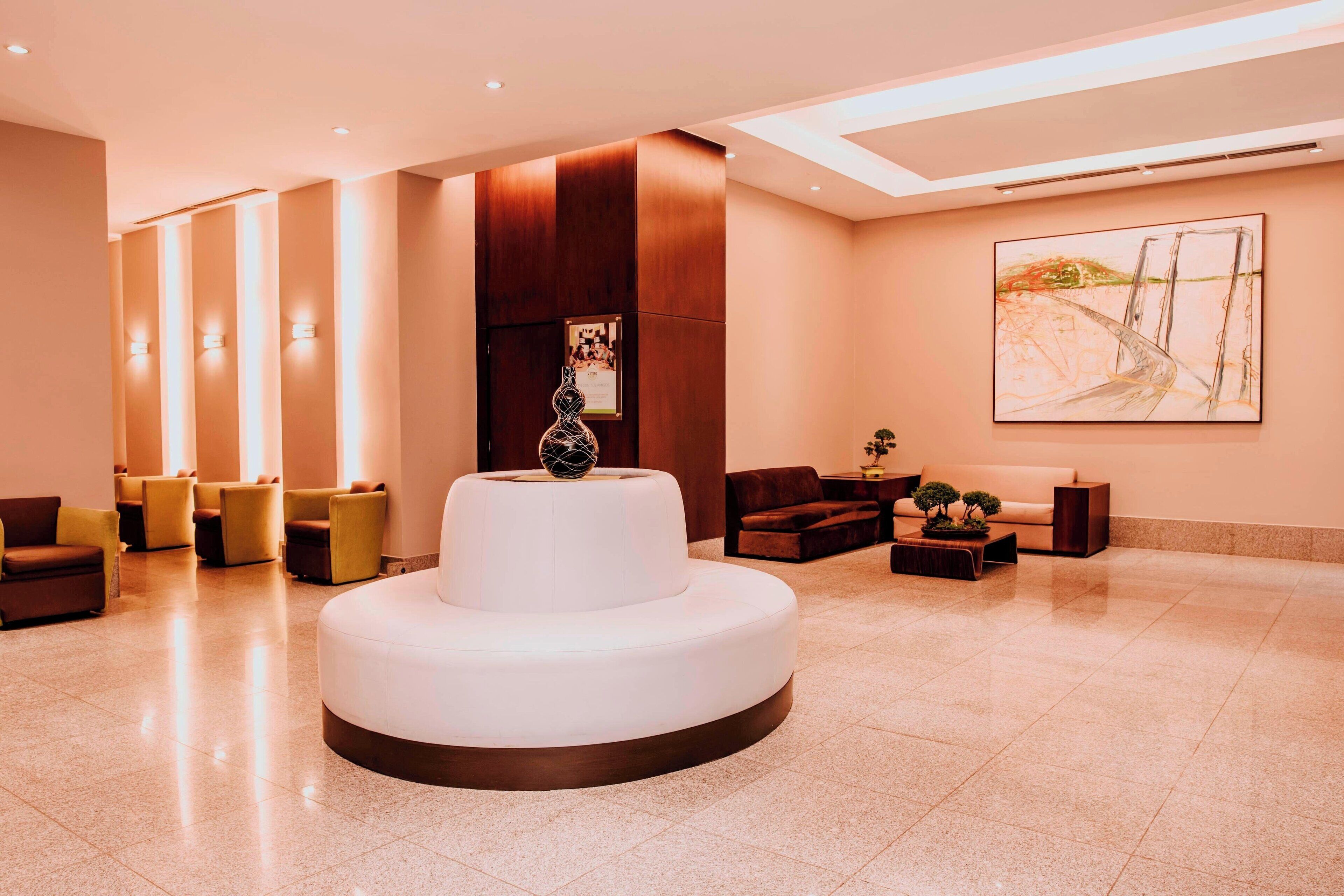 Eine moderne Lobby mit einer zentralen, weißen, runden Sitzecke, mehreren Sofas und einem großen, abstrakten Gemälde an der Wand.
