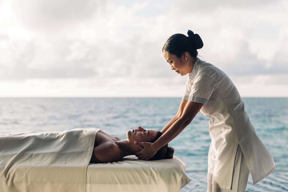 A person receiving a massage on a bed with a view of the ocean.