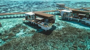 Overwater bungalows with private pools, connected by a wooden walkway, overlooking a clear turquoise sea and a white sandy beach. - Park Hyatt Maldives Hadahaa (Hadahaa)