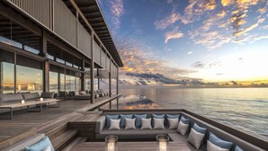 A modern outdoor deck with seating and candles, overlooking a body of water and a sunset sky. - Park Hyatt Maldives Hadahaa (Hadahaa)