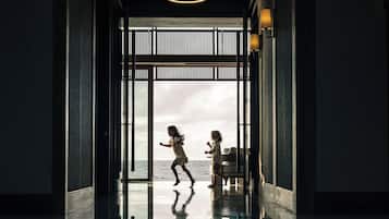 A modern interior with a reflective floor, a view of the sea through a large glass door, and a minimalist design with pendant lighting.