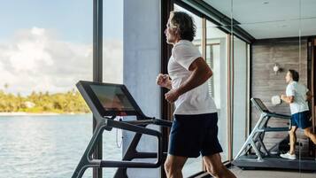 Un hombre corriendo en una caminadora con vista a una masa de agua y el reflejo de otra persona al fondo.