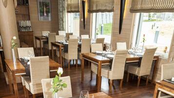 Un restaurant amb taules i caires de fusta, grans finestres i lluminàries penjants.