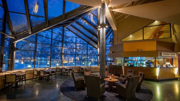 A spacious indoor area with large windows offering a view of snow-covered trees, a reception desk, and seating arrangements. - Hotel K5 Levi (Kittila)
