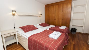 A hotel room with two beds, wooden wardrobe, white walls, and a small bedside table.
