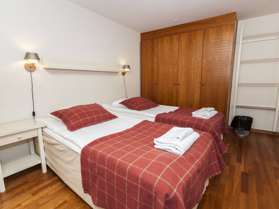 A hotel room with two beds, wooden wardrobe, white walls, and a small bedside table.