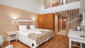 A modern hotel room with a wooden floor, a large bed with two pillows, a bedside table, a wardrobe, and a staircase leading to an upper level. - Hotel K5 Levi (Kittila)