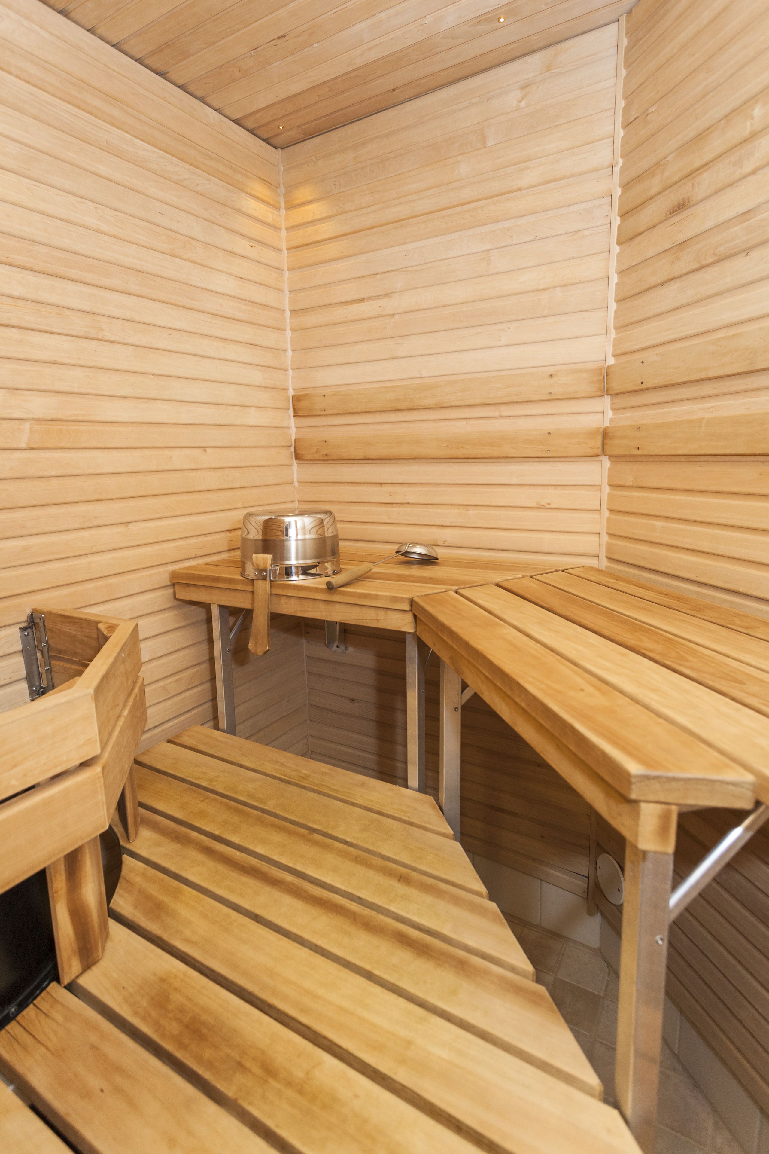 A sauna with wooden benches and a table, a metal container, and a small heater.