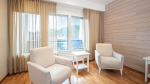 A modern living room with two beige armchairs, a small white table, and a large window with curtains. - Hotel K5 Levi (Kittila)