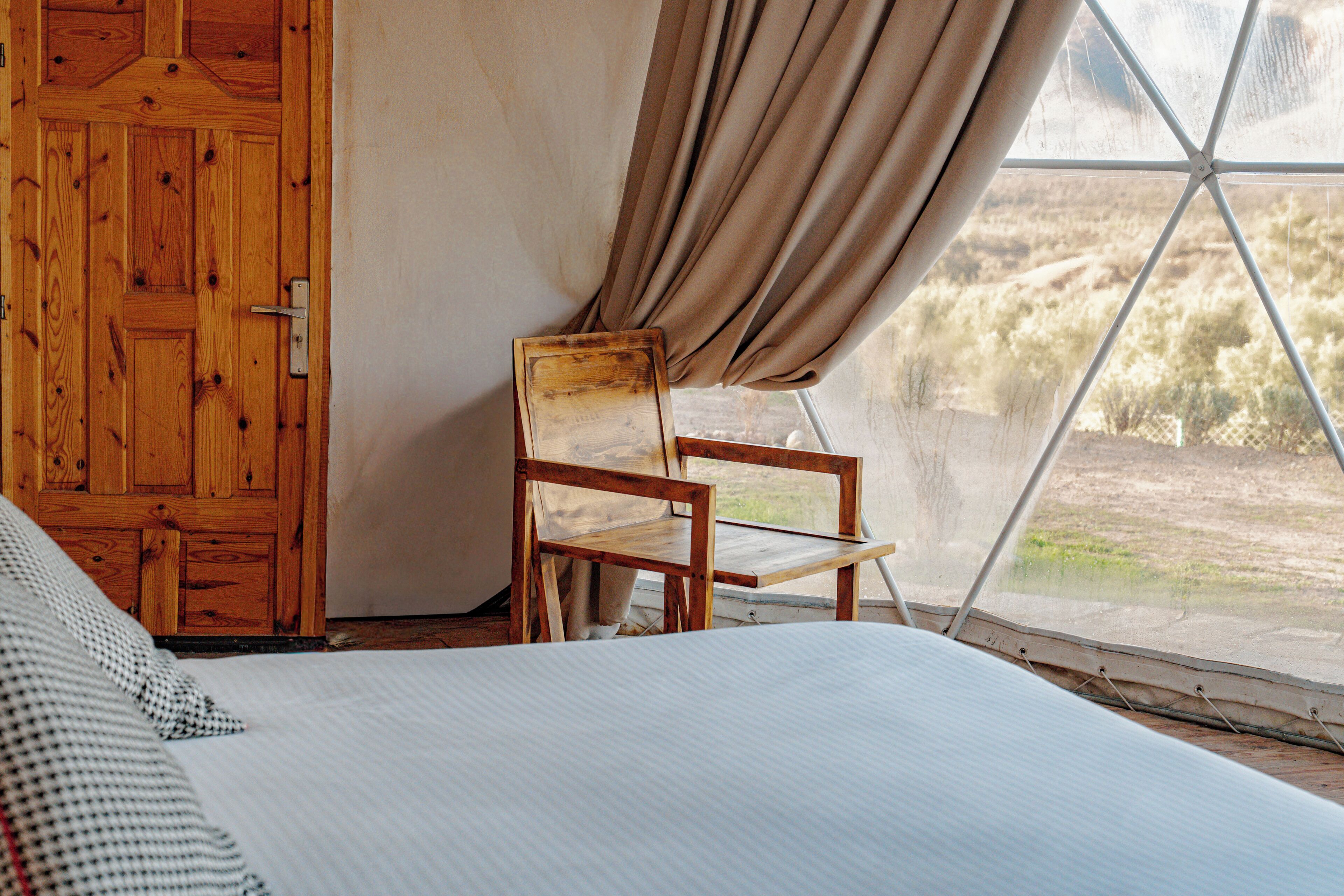 Un dormitorio con cama, una silla de madera y un ventanal con cortinas.