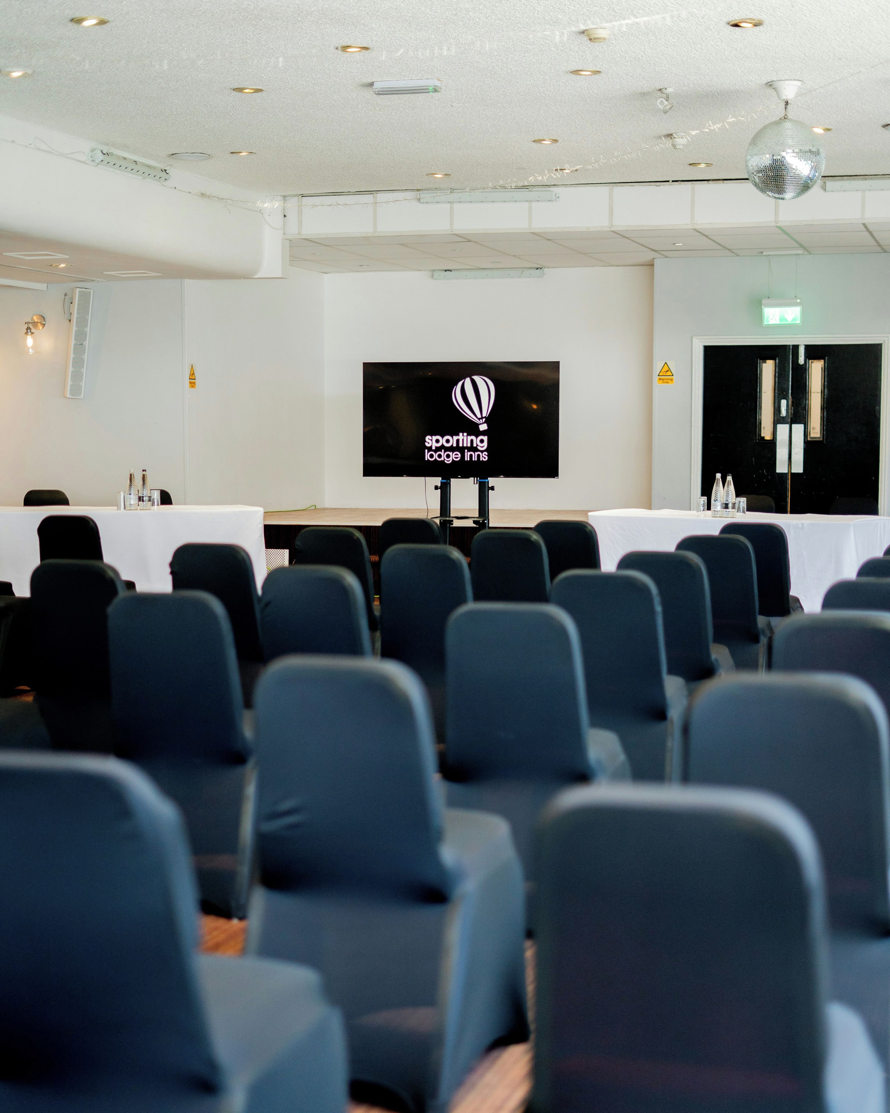 Un salón de conferencias con filas de sillas orientadas hacia una pantalla que muestra el logotipo de Sporting Lodges Inns.