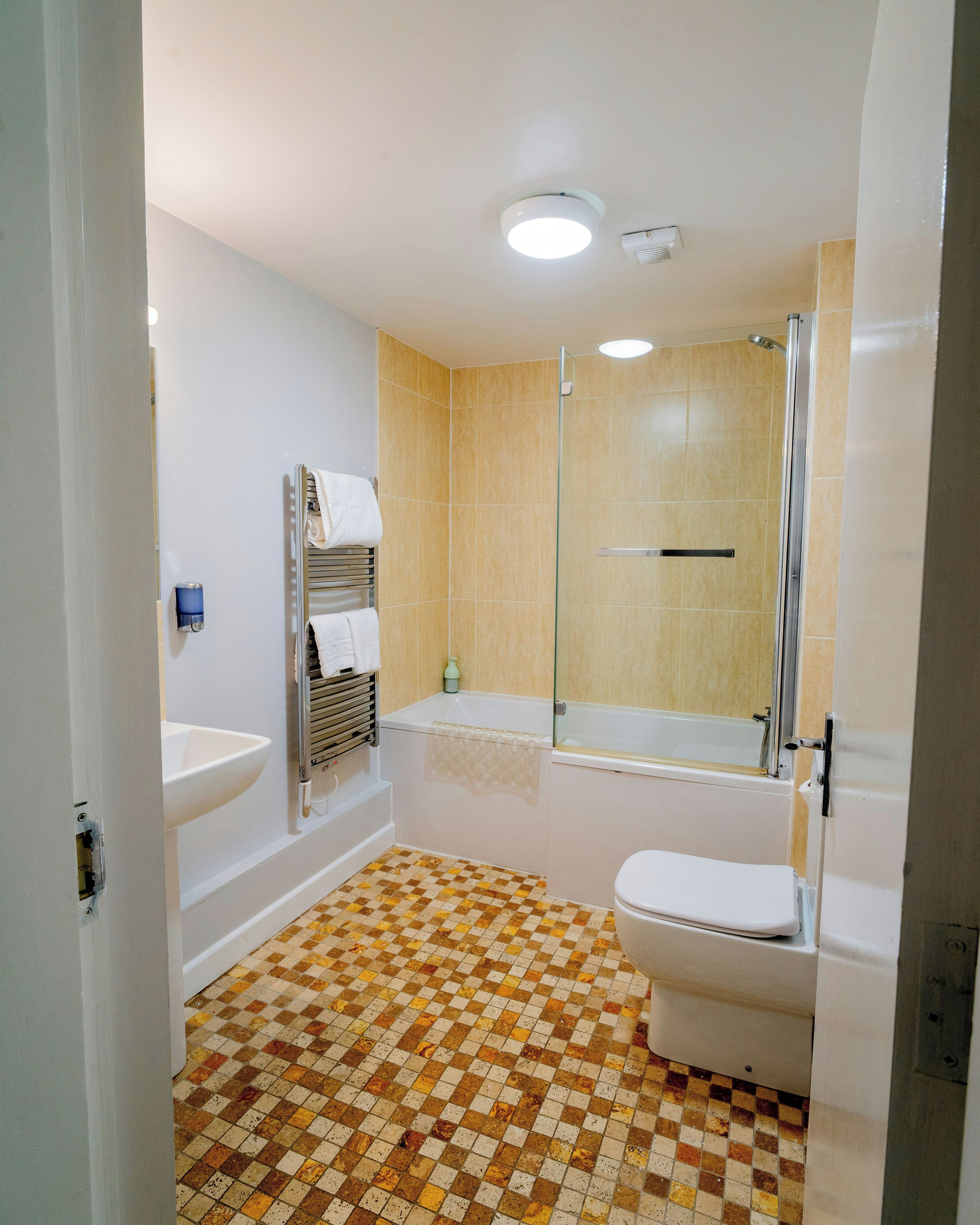 Ein Badezimmer mit Schachbrettboden, einer Badewanne, einer Toilette und einer gläsernen Duschkabine.