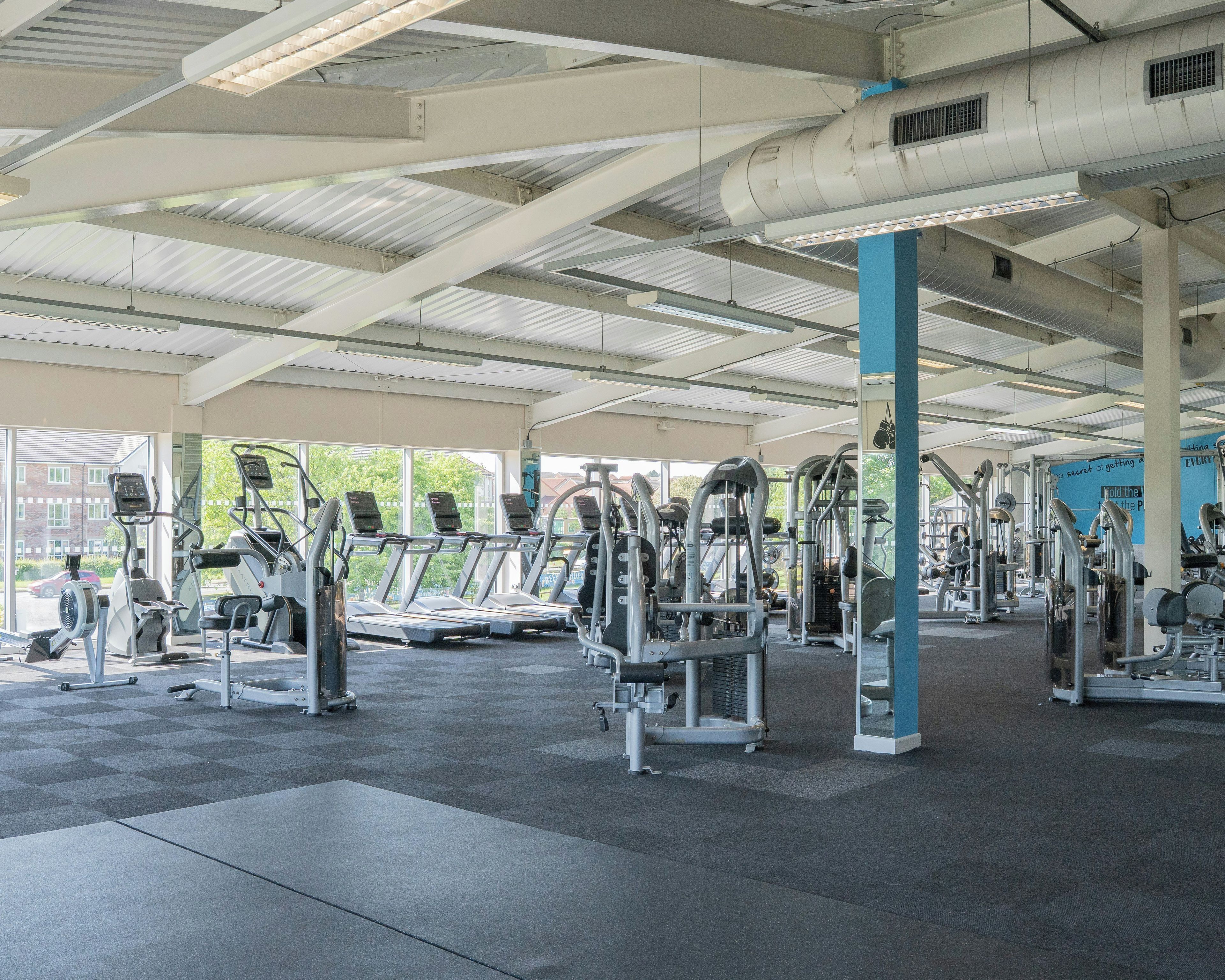 A gym with various exercise equipment, including treadmills and weight machines, under a covered area with a view of the outside.