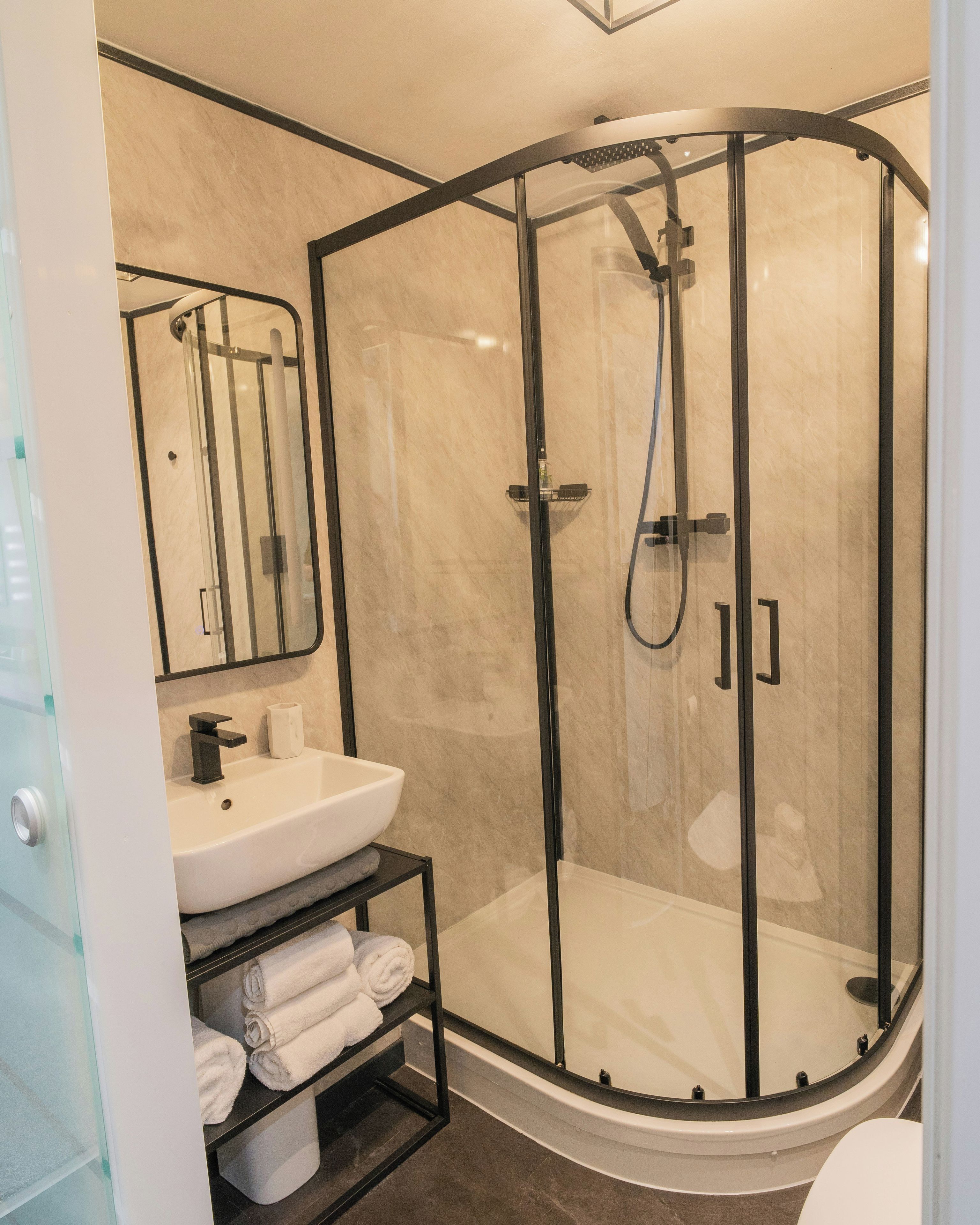 Un baño moderno con ducha envuelta en vidrio, un lavamanos blanco y un perchero para toallas.