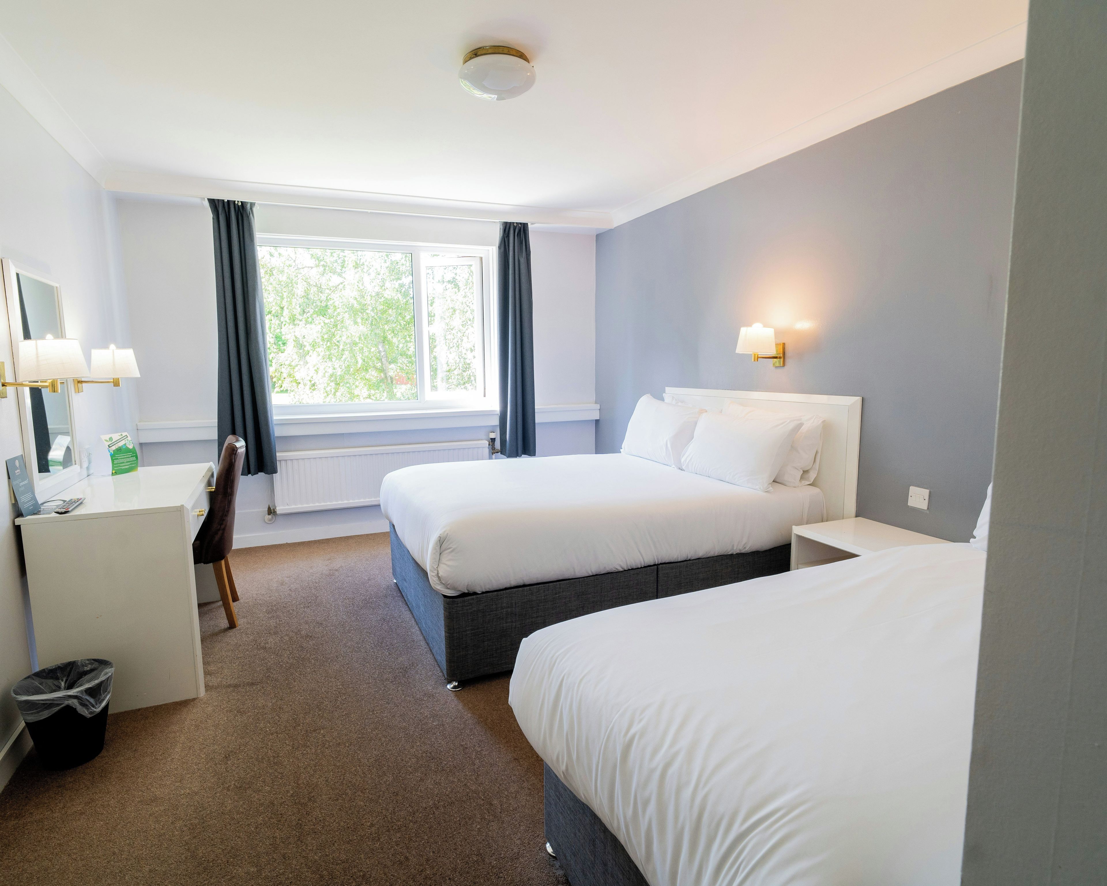 A hotel room with a bed, a desk, a chair, and a window with curtains.