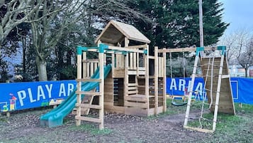 A wooden play structure with a slide and climbing area, surrounded by trees and a blue banner with 'PLAY AREA' text.