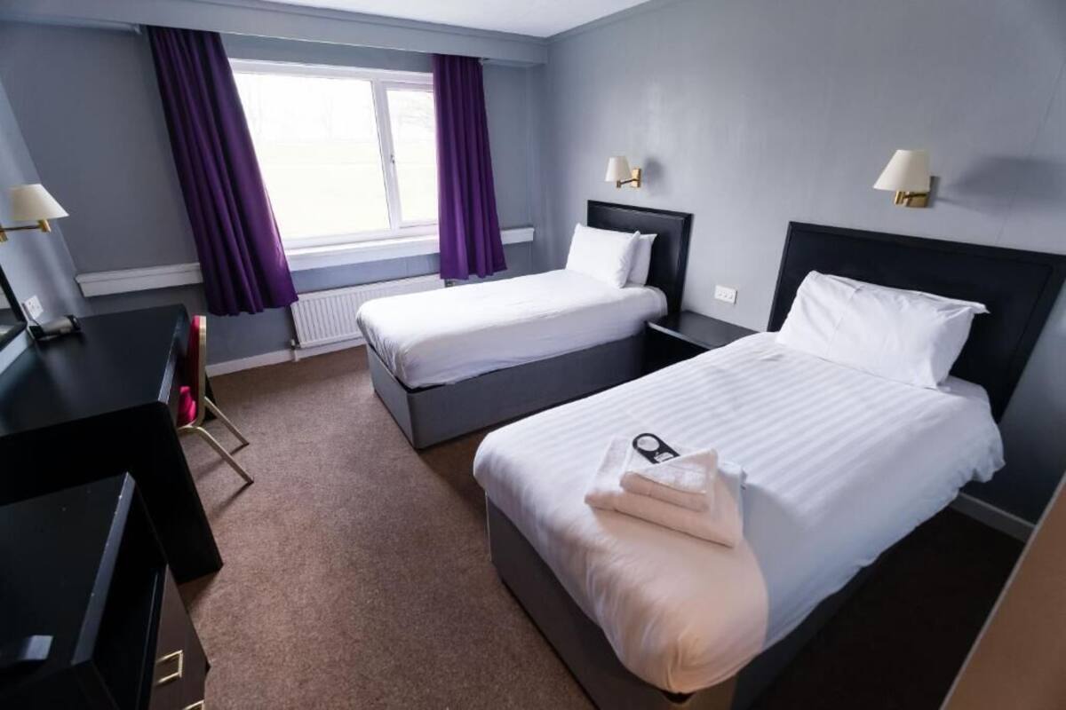 A hotel room with two beds, a desk, and a chair.