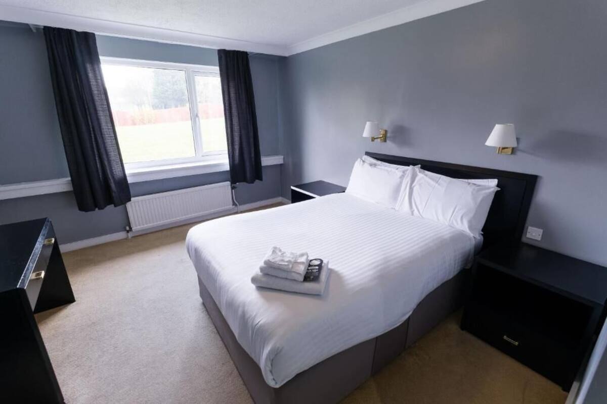 A hotel room with a large bed, two bedside tables, a window with curtains, and a radiator.