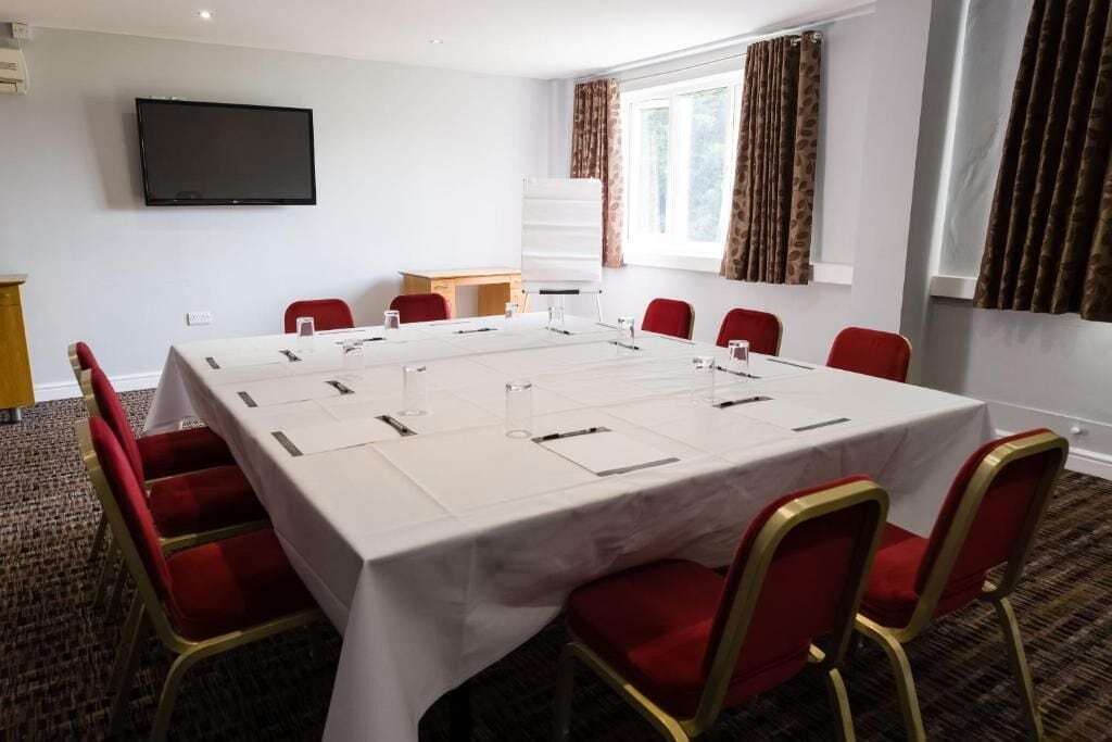 A conference room with a large table, red chairs, a whiteboard, and a television on the wall.