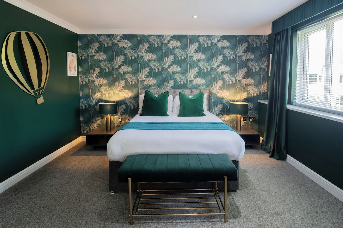 A hotel room with a large bed, two bedside tables, a green accent wall, and a window with curtains.