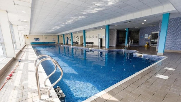 Piscina interior com água cristalina, escada de metal e paredes azulejadas.