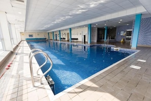 Ein Hallenbad mit klarem Wasser, einer Metallleiter und gefliesten Wänden.