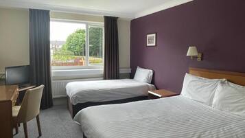 Une chambre d’hôtel avec deux lits, un bureau, une chaise, une fenêtre avec des rideaux et une lampe fixée au mur.