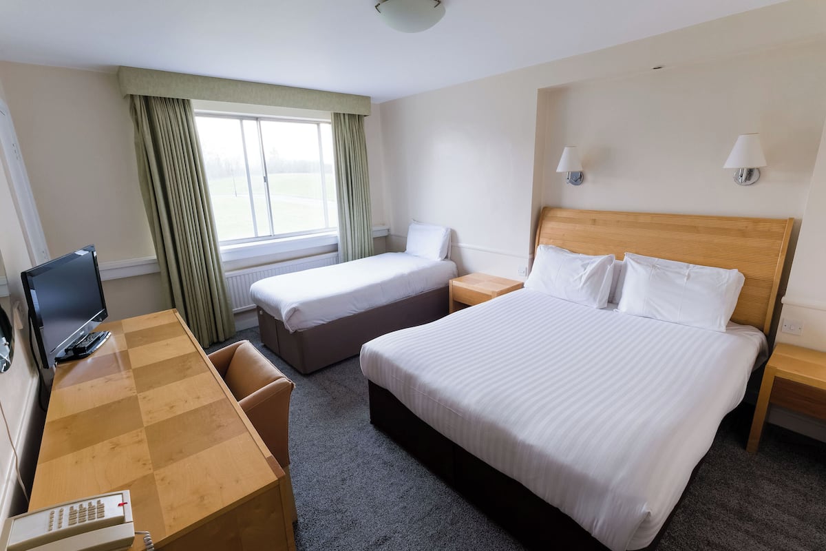 A hotel room with a large bed, a smaller bed, a desk with a computer, a chair, and a window with curtains.