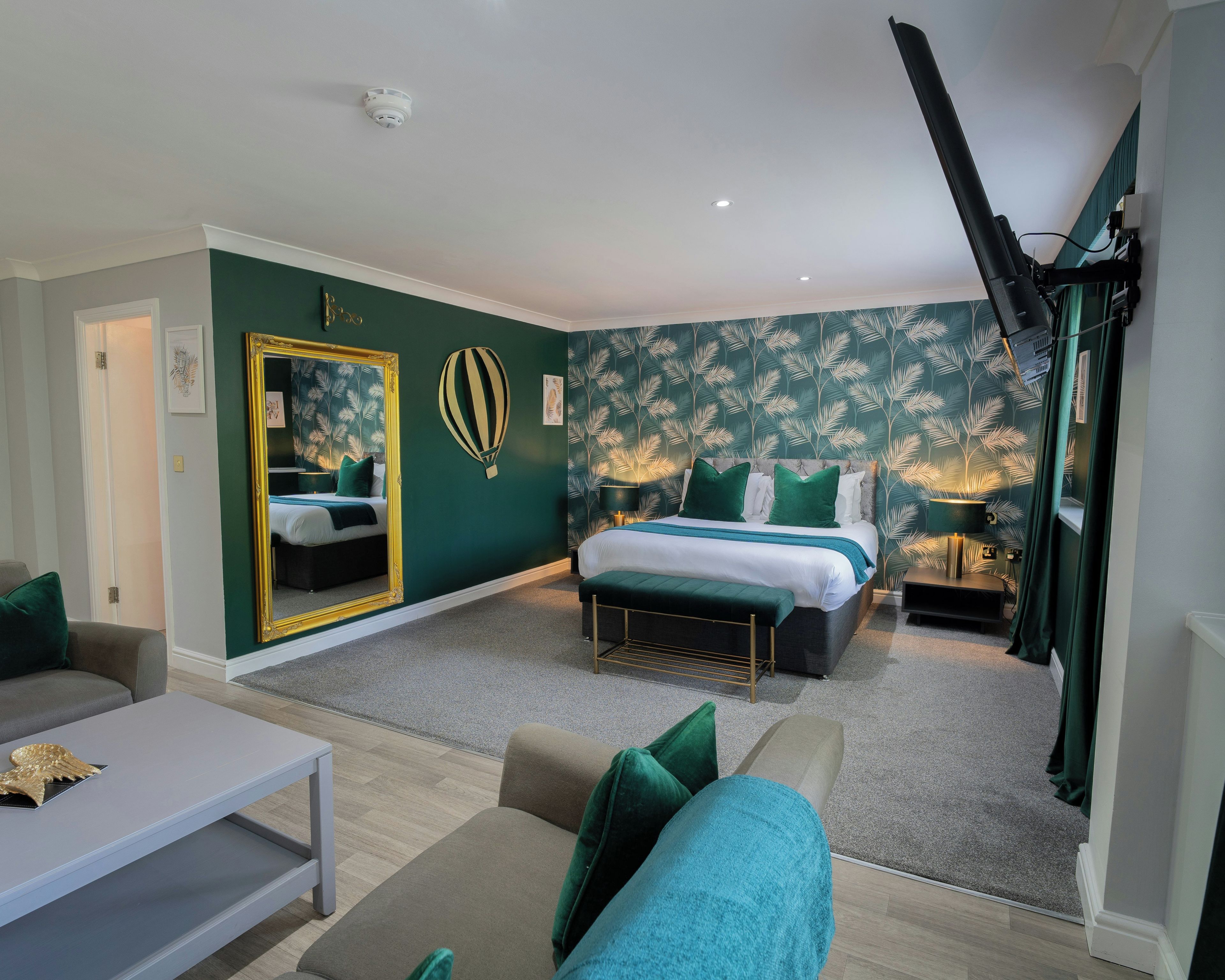 A modern bedroom with a large bed, a sitting area with a sofa and a coffee table, and a mirror with a decorative frame.