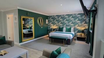 Un dormitorio moderno con una cama grande, una zona de estar con un sofá y una mesa de centro, y un espejo con un marco decorativo.
