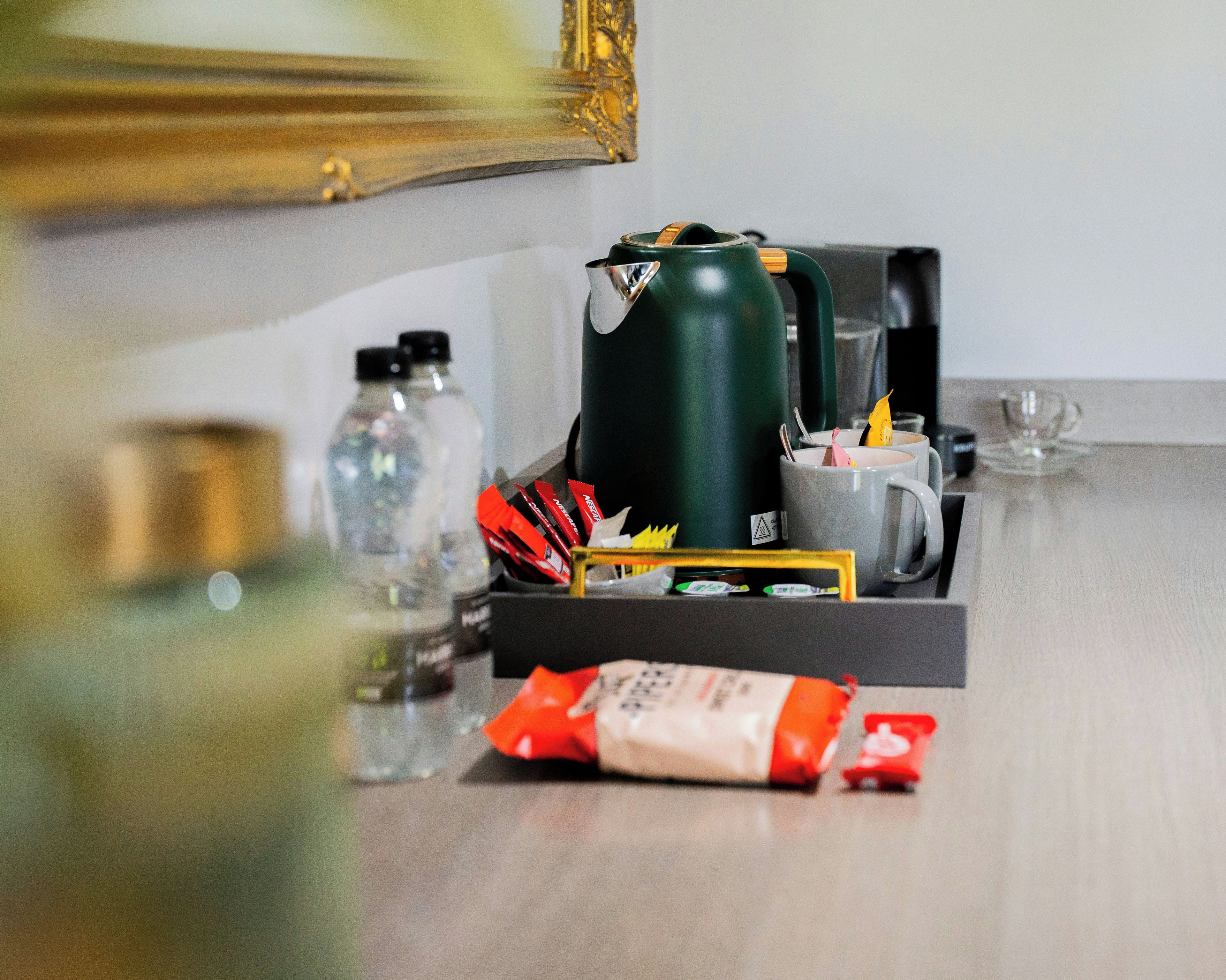 En kaffebryggare, en vattenkokare, en mugg, ett glas och en förpackning med kaffegrädde står på en bänkskiva.