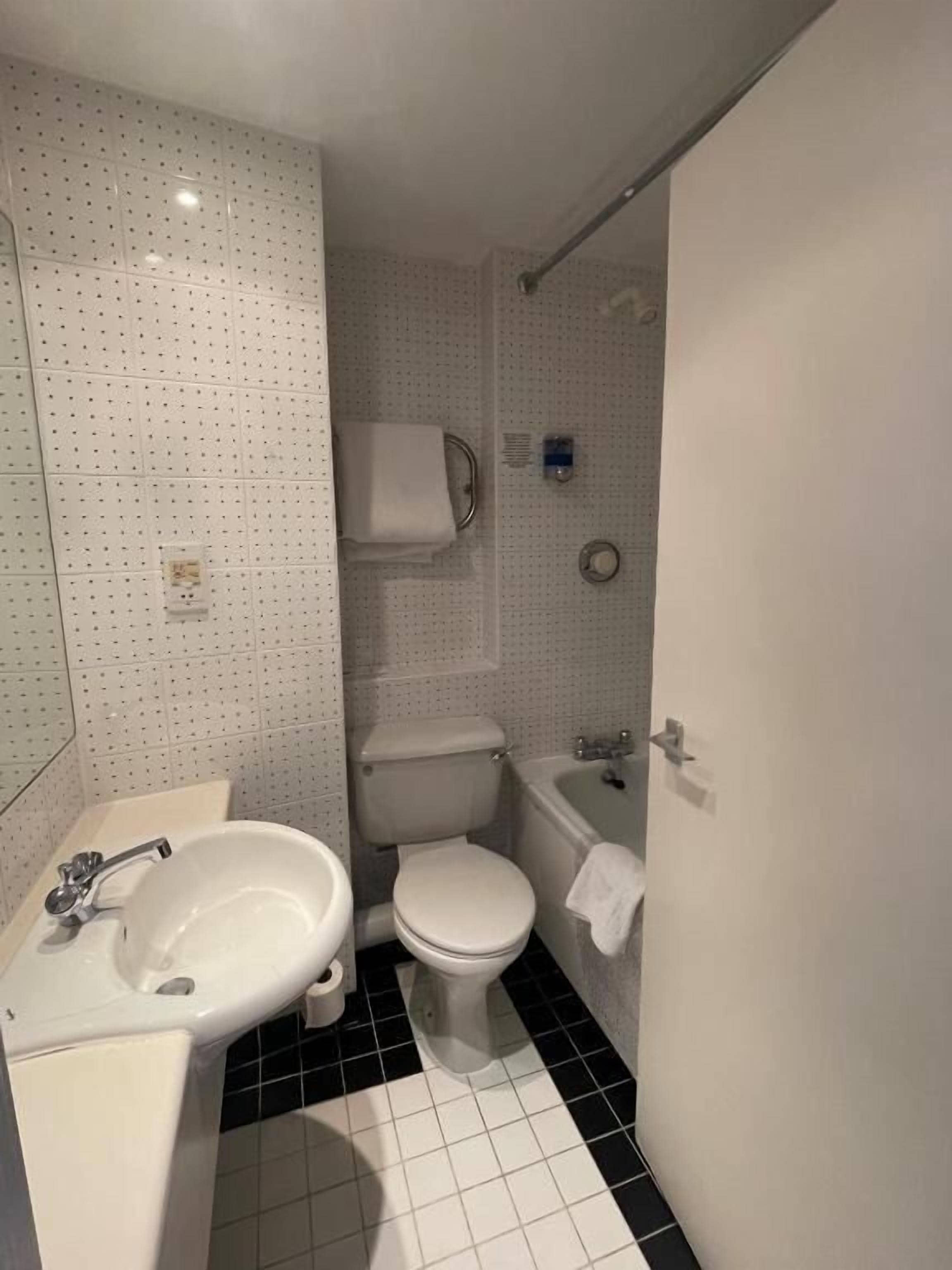 A bathroom with a white sink, toilet, and bathtub, tiled floor, and a shower curtain rod.