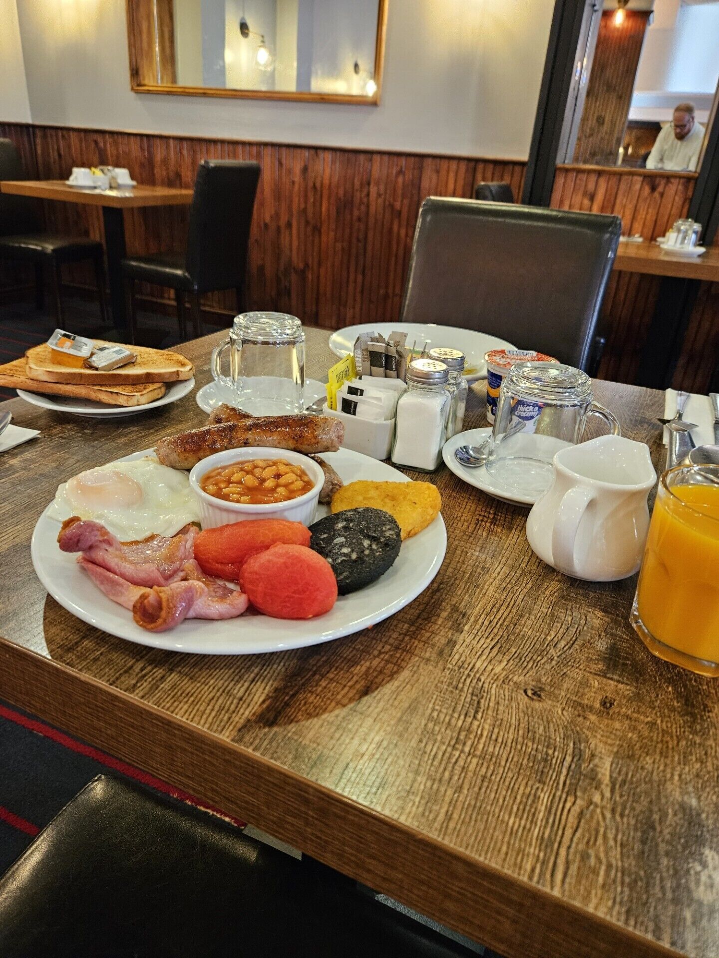 Une table de petit-déjeuner avec des toasts, des œufs, des saucisses, des haricots et une variété de condiments.