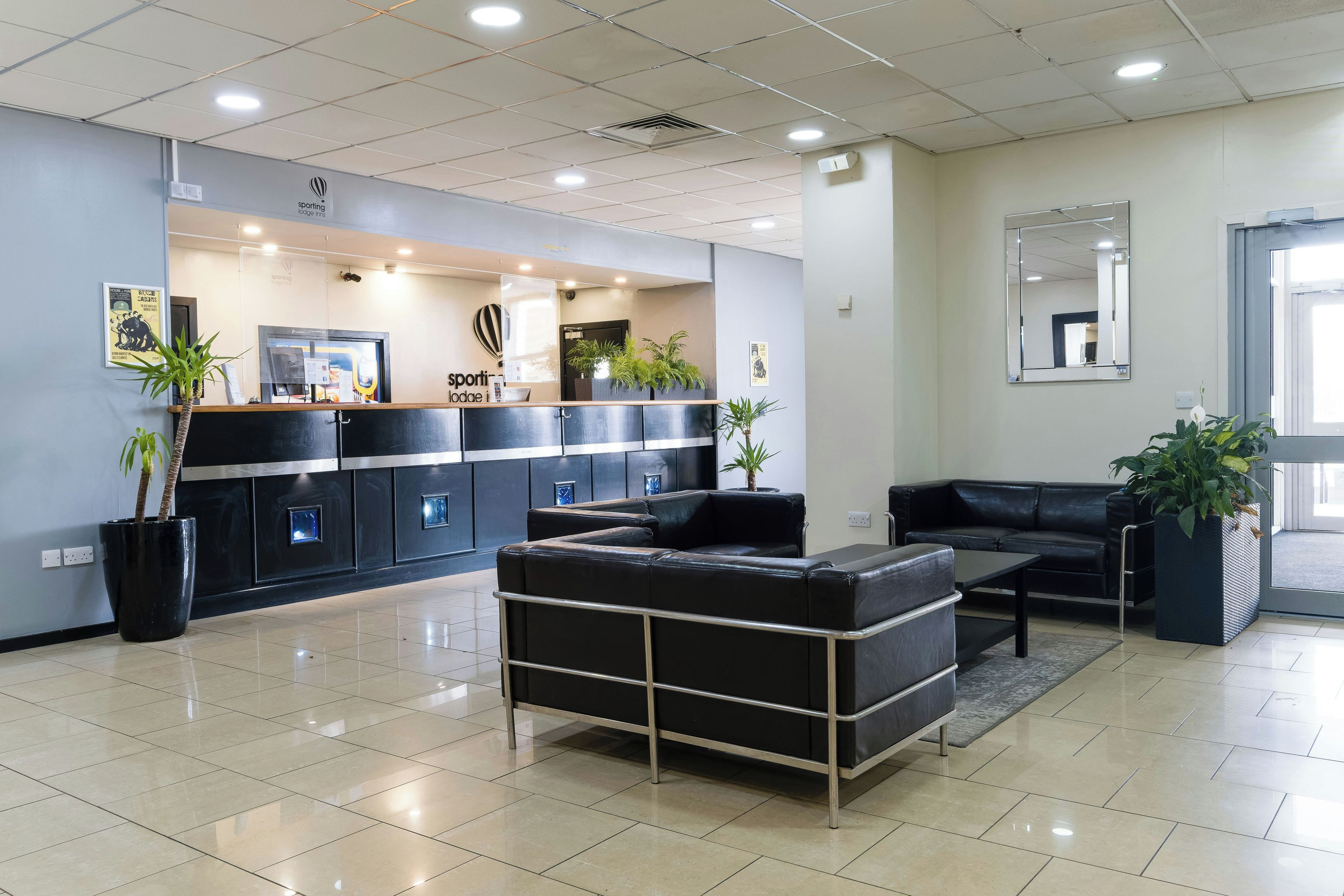 Un moderno vestíbulo de hotel con mostrador de recepción, zona de estar y un espejo grande.