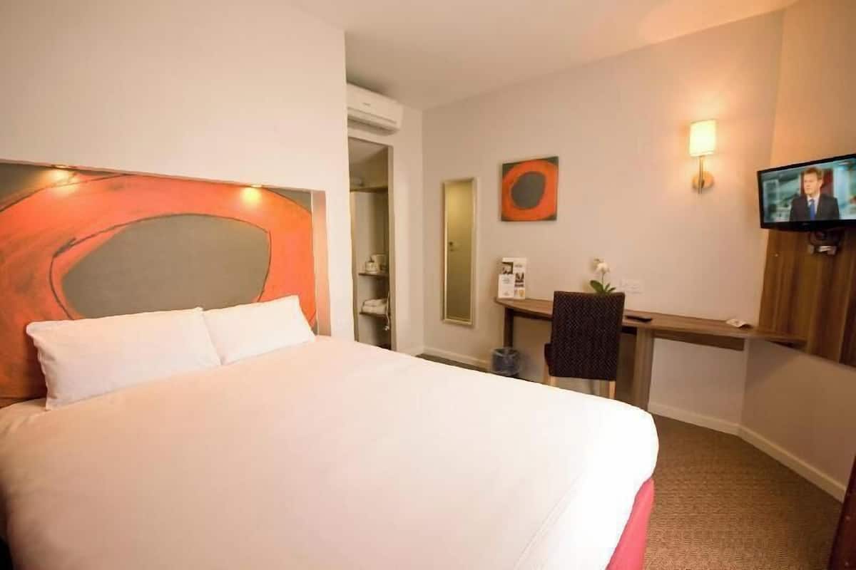 A hotel room with a bed, a desk, a television, and a wall-mounted artwork.