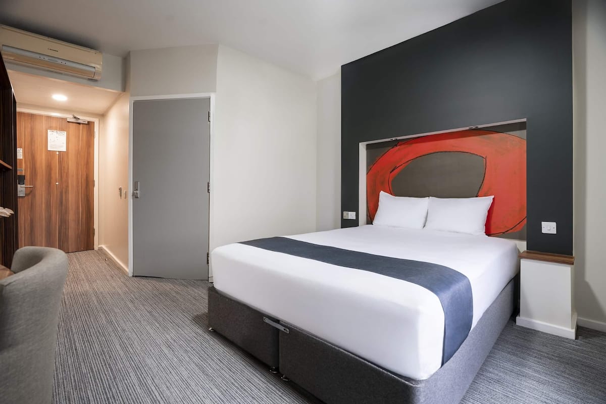 A hotel room with a large bed, a grey carpet, a wooden door, and a modern wall art piece.